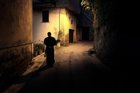 Ein Priester läuft durch eine beleuchtete Gasse