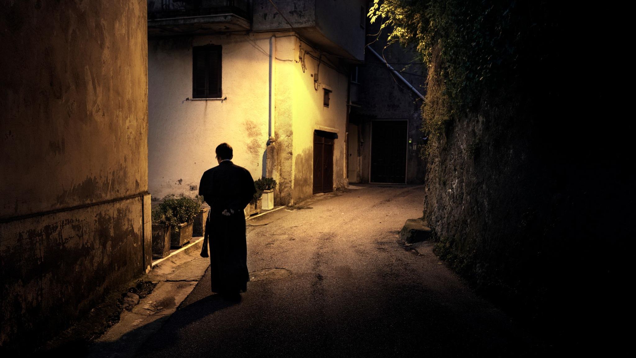 Ein Priester läuft durch eine beleuchtete Gasse