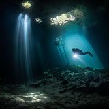 Eine tauchende Person im Lichtstrahl einer Öffnung der Calvera Cenote