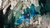 Eine tauchende Person taucht durch einen Durchgang in der Gran Cenote
