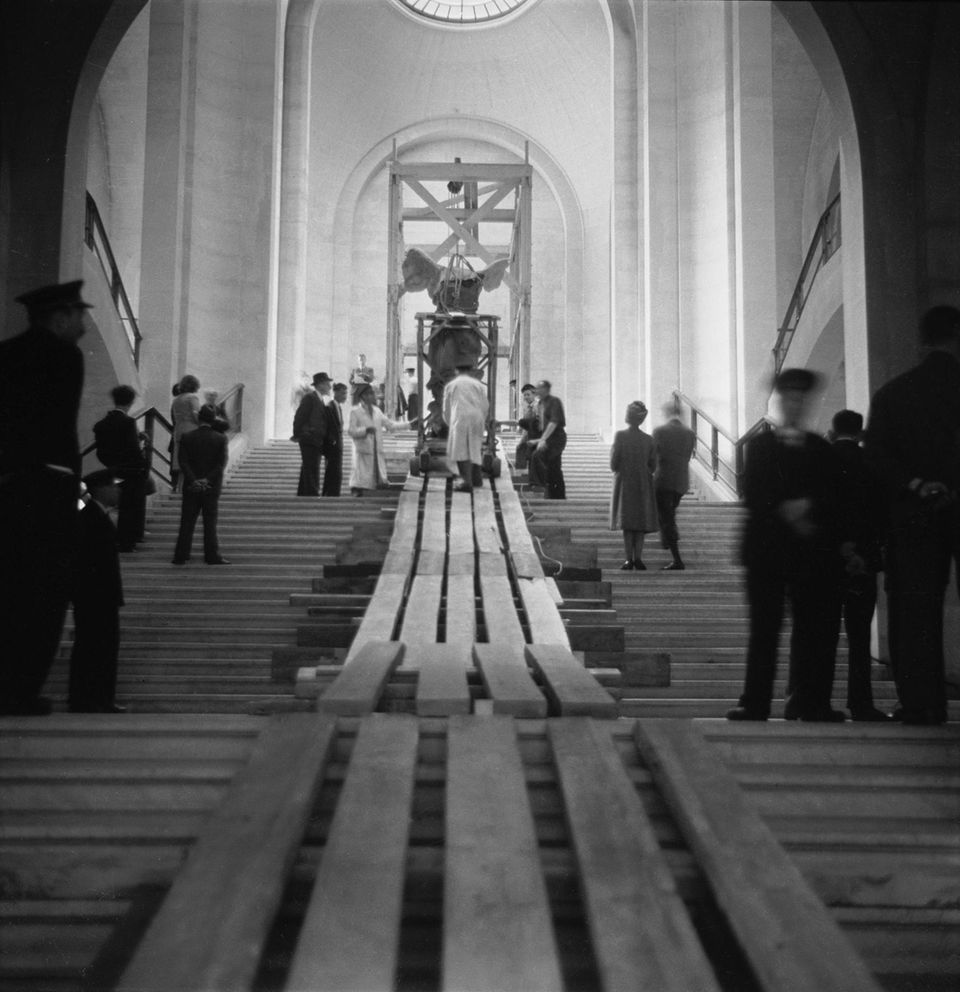 Mitte Juni 1945 schieben Mitarbeiter die in Sackleinen gehüllte und an Seilen und Kabeln aufgehängte griechische Marmorstatue "Nike von Samothrake" eine Rampe im Louvre empor an ihren angestammten Platz. Die geflügelte Siegesgöttin krönt bis heute die monumentale Daru-Treppe des Pariser Museums