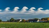 Wolkenwellen im Wind Wellenförmige Wolken ziehen über eine Ortschaft mit Feld