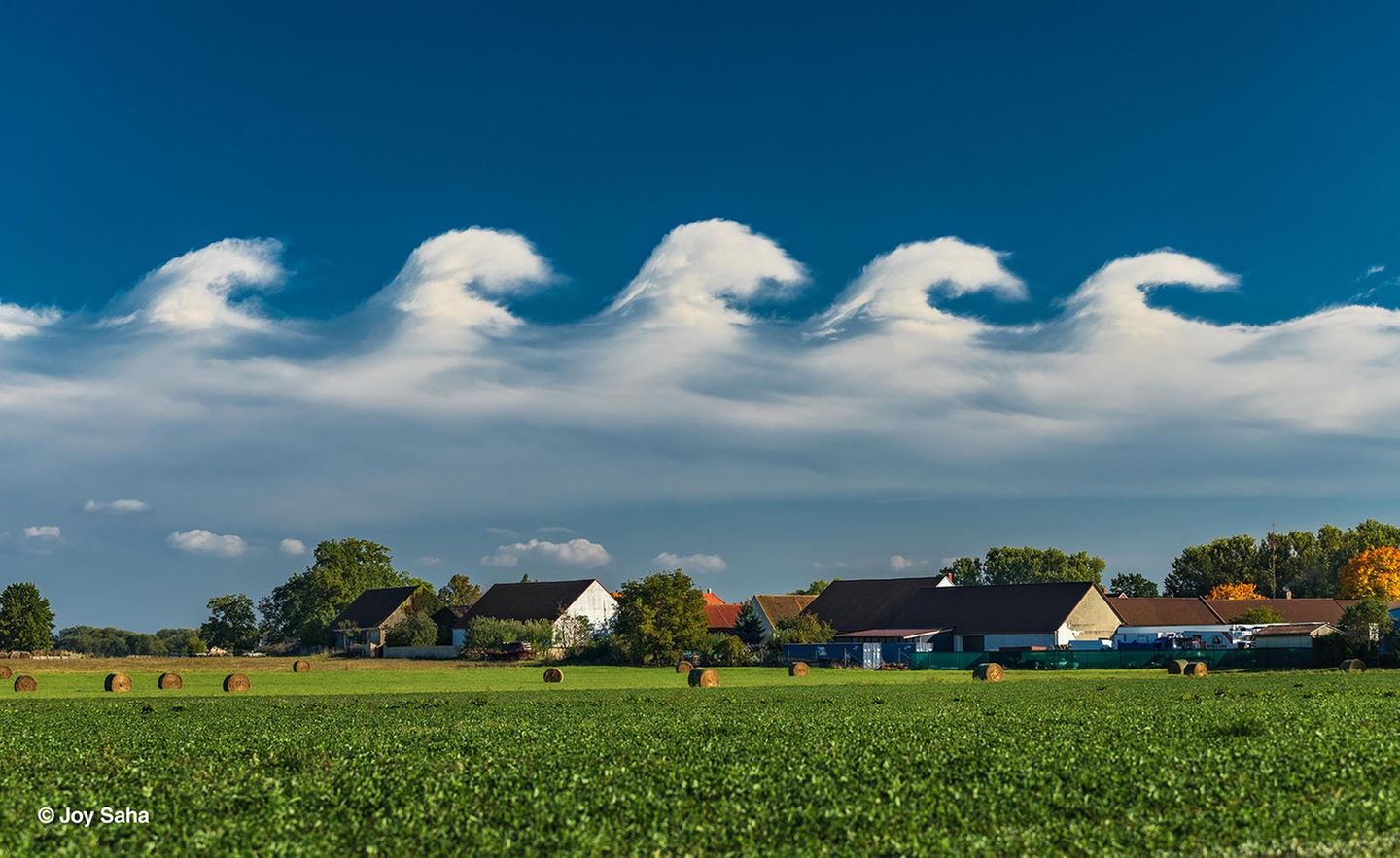 Wolkenwellen im Wind Wellenförmige Wolken ziehen über eine Ortschaft mit Feld