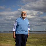 EIn Mann steht auf einem Feld, im Hintergrund sind Windräder zu sehen