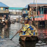 Eine Frau rudert in einem Boot durch eine Stelzenhaussiedlung