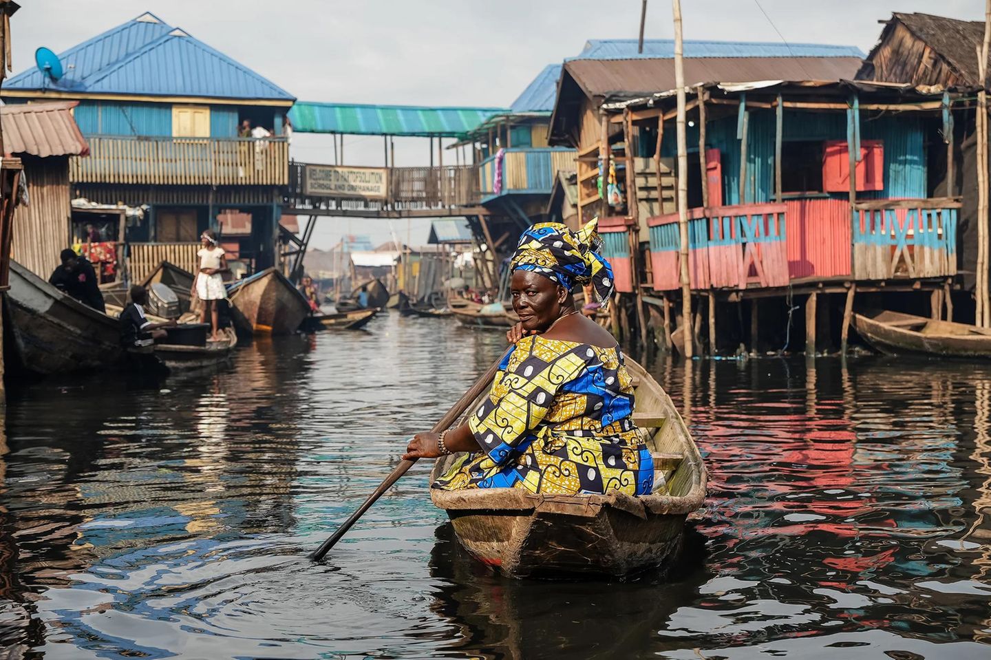 Eine Frau rudert in einem Boot durch eine Stelzenhaussiedlung