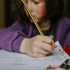 Kind hält einen Bleistift über einem Schulheft