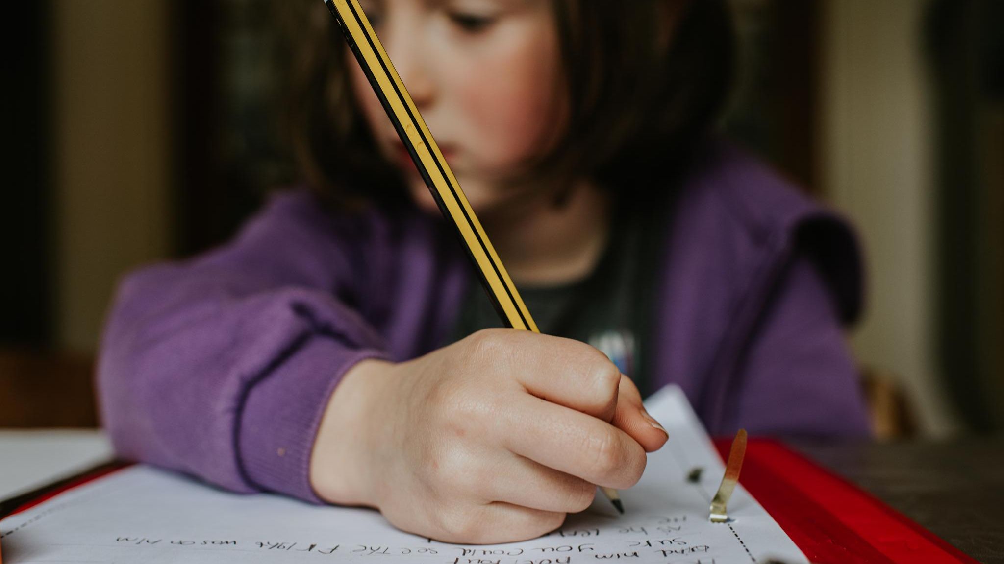 Kind hält einen Bleistift über einem Schulheft