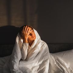 Eine Frau ist in eine Decke gehüllt und hält sich verschlafen den Kopf