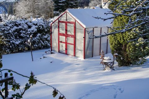 Ein Gewächshaus im Winter mit viel Schnee im Garten