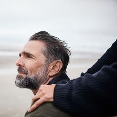 Ein Mann am Strand mit den Händen einer Frau auf seinen Schultern