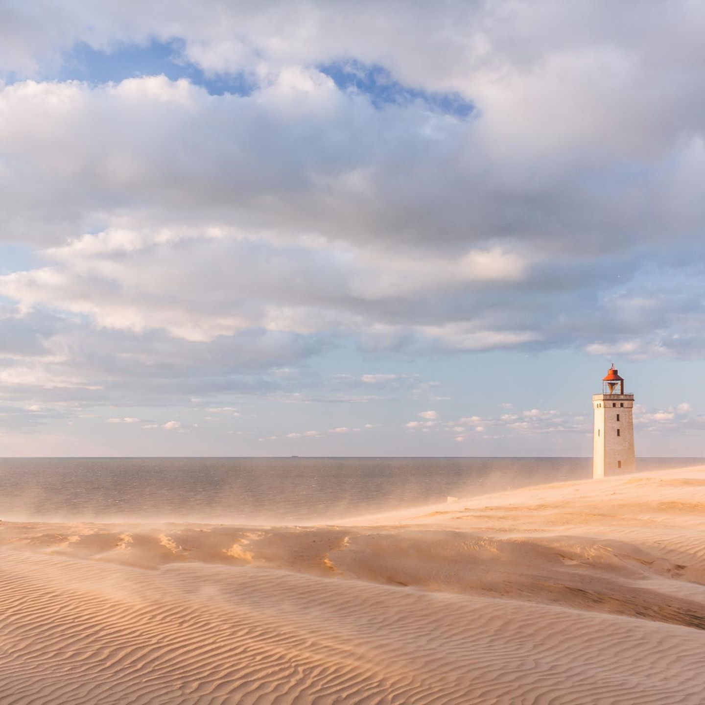 Nahe dem kleinen Ort Lønstrup an der nordjütischen Westküste finden Reisende eine wahre Ikone: den Leuchtturm von Rubjerg Knude. Schon von Weitem sichtbar, thront er auf einer der größten Wanderdünen Europas und ist eines der bekanntesten Wahrzeichen Nordjütlands. Einst 200 Meter von der Küste entfernt errichtet, kämpft er bis heute gegen die beständige Kraft von Wind, Sand und Meer. Im Oktober 2019 wurde der 23 Meter hohe Turm deshalb spektakulär um 80 Meter landeinwärts versetzt, weil die stetige Erosion ihn an den Rand der Steilküste gedrängt hatte. Wer den Turm erklimmt, wird mit einem atemberaubenden Ausblick über die raue See und die Steilküste belohnt. 