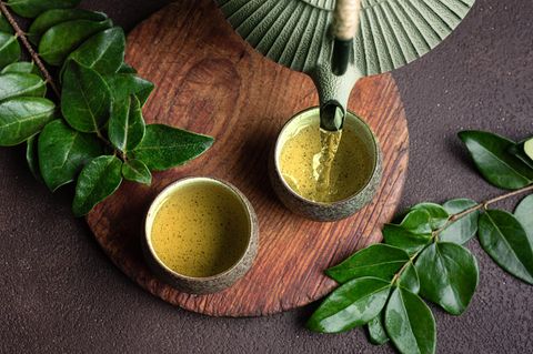 Grüner Tee wird aus einer Kanne in eine Schale eingeschenkt