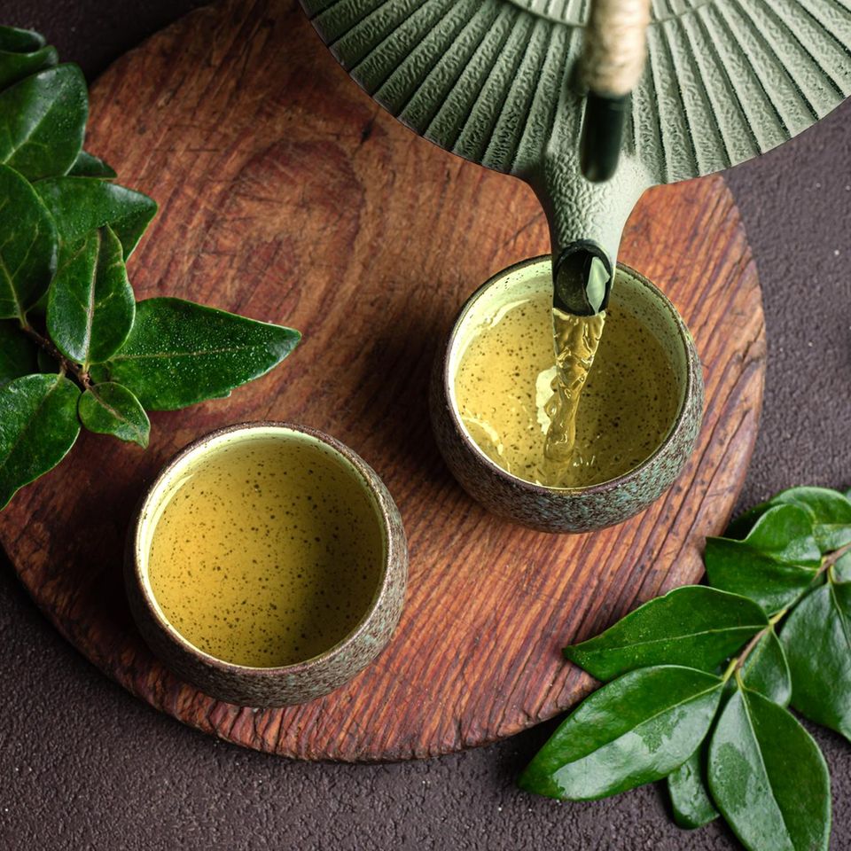 Grüner Tee wird aus einer Kanne in eine Schale eingeschenkt