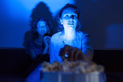 Zwei Freundinnen im blauen Fernsehlicht schauen mit Anspannung im Gesicht einen Film und fiebern mit