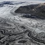 Wenn sich Gletscherströme ihren Weg durch das Gebirge bahnen, verschlägt ihre schiere Kraft den Betrachtenden meist den Atem. Die schwarze Vulkanasche, die das Eis des Skeidararjökull hier marmoriert, zeugt jedoch von einem noch gewaltigeren Naturspektakel: dem Wechselspiel zwischen Schnee und Feuer, Sonne und Wind. "Die Vulkaneruptionen liefern die schwarze Asche, welche die Gletscher überdeckt. Darauf fällt frischer Schnee, der allmählich zu Eis komprimiert wird. So legt sich weiße auf schwarze Schicht, viele Male", beschreibt die Geologin Angelika Jung-Hüttl das Phänomen. Je weiter sich der Gletscher seinen Weg ins Tal bahnt, desto verwobener sind die beiden Schichten, desto schwungvoller die Muster.