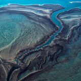 50 Arten Türkis: So leuchtet das Wasser des Montgomery Riff vor der Nordwestküste Australiens. Die Strahlkraft verändert sich je nach Wasserstand, der Tidehub zwischen Niedrigwasser und Hochwasser beträgt hier rund zehn Meter: Bei Ebbe ragt das Riff aus dem Wasser, bei Flut verschwindet es komplett. "Bei Flut liegen Riffplattform und Gezeitenkanal – gleichmäßig überspült– knapp unter dem Meeresspiegel. Bei Ebbe jedoch, wenn der Meeresspiegel innerhalb weniger Stunden tief fällt, fließt das Wasser schneller aus dem großen Gezeitenkanal ab, als es von der Plattform nachfließen kann", schreibt die Geographin Angelika Jung-Hüttl. Dann stürzt es dem Kanal in Wasserfällen über die Riffkante entgegen, die das Riff von oben betrachtet mit Narben übersäen. Der spektakuläre Anblick bleibt den Riffbewohnern verborgen, die sich im vom Gezeitenwechsel bestimmten Lebensraum tummeln: Meeresschildkröten, Wale, Riffhaie, Mantarochen und Salzwasserkrokodile. 