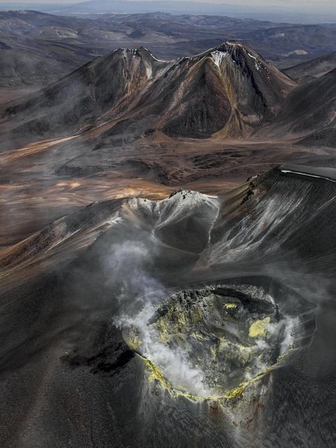 Wie eine eiternde Wunde klafft der Vulkankrater auf dem Gipfel des Isluga, der sich über der kahlen Landschaft des Altiplano an der Grenze zwischen Chile und Bolivien erhebt. Gasschwaden treten aus seinem Inneren; gelb gefärbtes Gestein an den Kraterwänden bezeugt die Schwefelvorkommen, die hier vor einigen Jahrzehnten noch abgebaut wurde. Bernhard Edmaier fotografierte den gewaltigen Krater mit einem Durchmesser von 400 Metern aus der Vogelperspektive und dabei Wissenschaft und Kunst vereint. Der Fotograf und Geologe zeigt mit seinen spektakulären Luftaufnahmen im Bildband "Elements", mit welcher Macht die Natur Landschaften formt – nicht nur hier, in der Hochebene der Anden, sondern auf allen Kontinenten.  