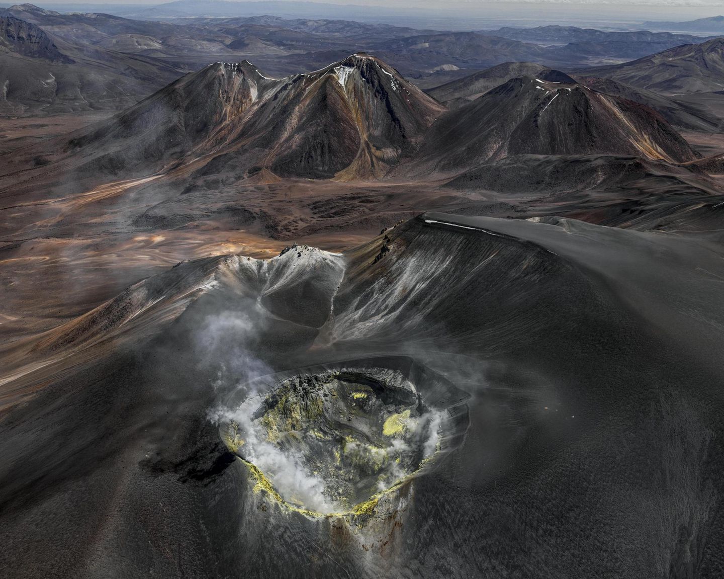 Wie eine eiternde Wunde klafft der Vulkankrater auf dem Gipfel des Isluga, der sich über der kahlen Landschaft des Altiplano an der Grenze zwischen Chile und Bolivien erhebt. Gasschwaden treten aus seinem Inneren; gelb gefärbtes Gestein an den Kraterwänden bezeugt die Schwefelvorkommen, die hier vor einigen Jahrzehnten noch abgebaut wurde. Bernhard Edmaier fotografierte den gewaltigen Krater mit einem Durchmesser von 400 Metern aus der Vogelperspektive und dabei Wissenschaft und Kunst vereint. Der Fotograf und Geologe zeigt mit seinen spektakulären Luftaufnahmen im Bildband "Elements", mit welcher Macht die Natur Landschaften formt – nicht nur hier, in der Hochebene der Anden, sondern auf allen Kontinenten.  