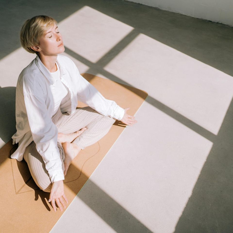 weiß gekleidete Frau von oben fotografiert meditiert im Sonnenlicht