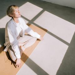 weiß gekleidete Frau von oben fotografiert meditiert im Sonnenlicht