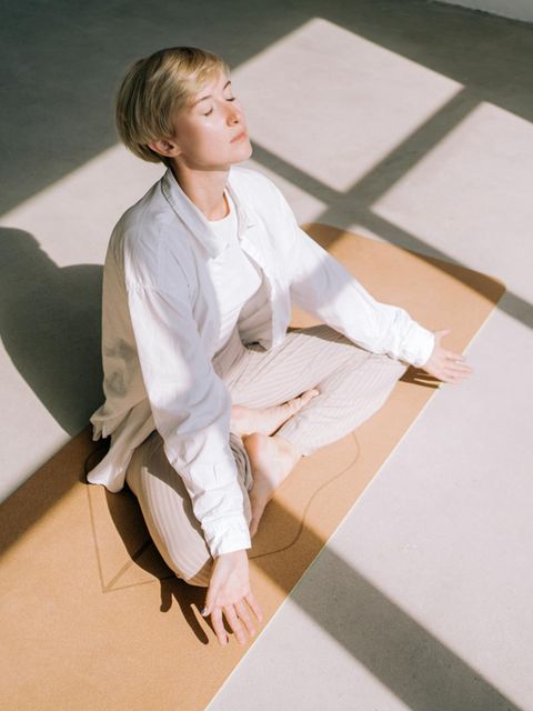 weiß gekleidete Frau von oben fotografiert meditiert im Sonnenlicht