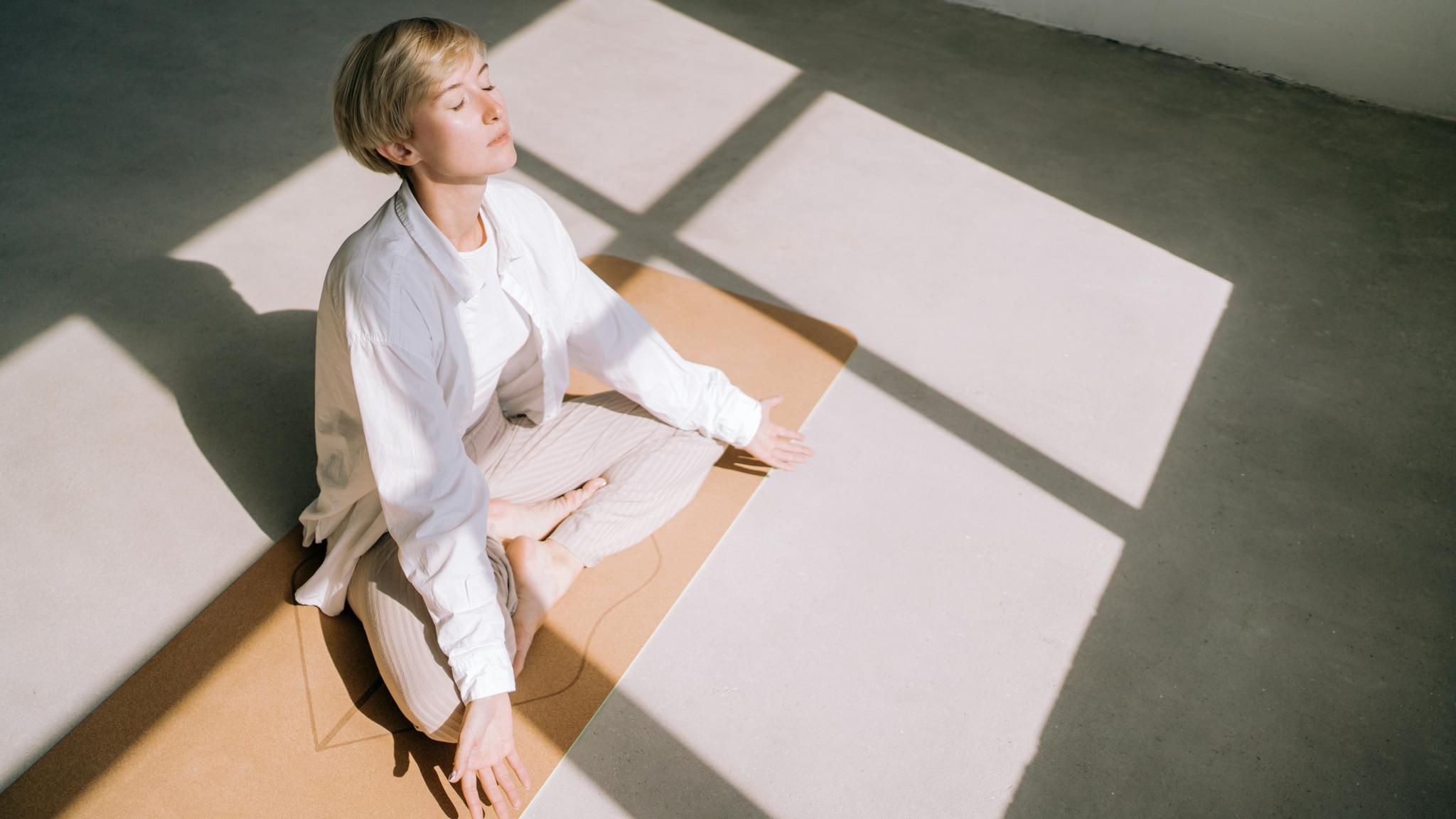 weiß gekleidete Frau von oben fotografiert meditiert im Sonnenlicht