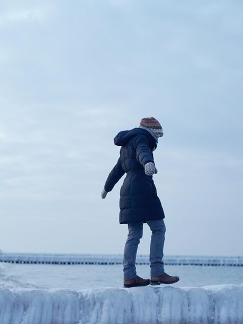 Frau balanciert unsicher auf einer glatten Buhne aus Eis am Meer