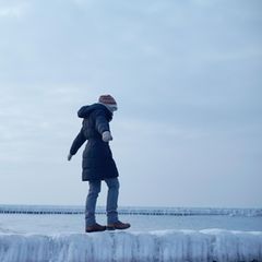 Frau balanciert unsicher auf einer glatten Buhne aus Eis am Meer