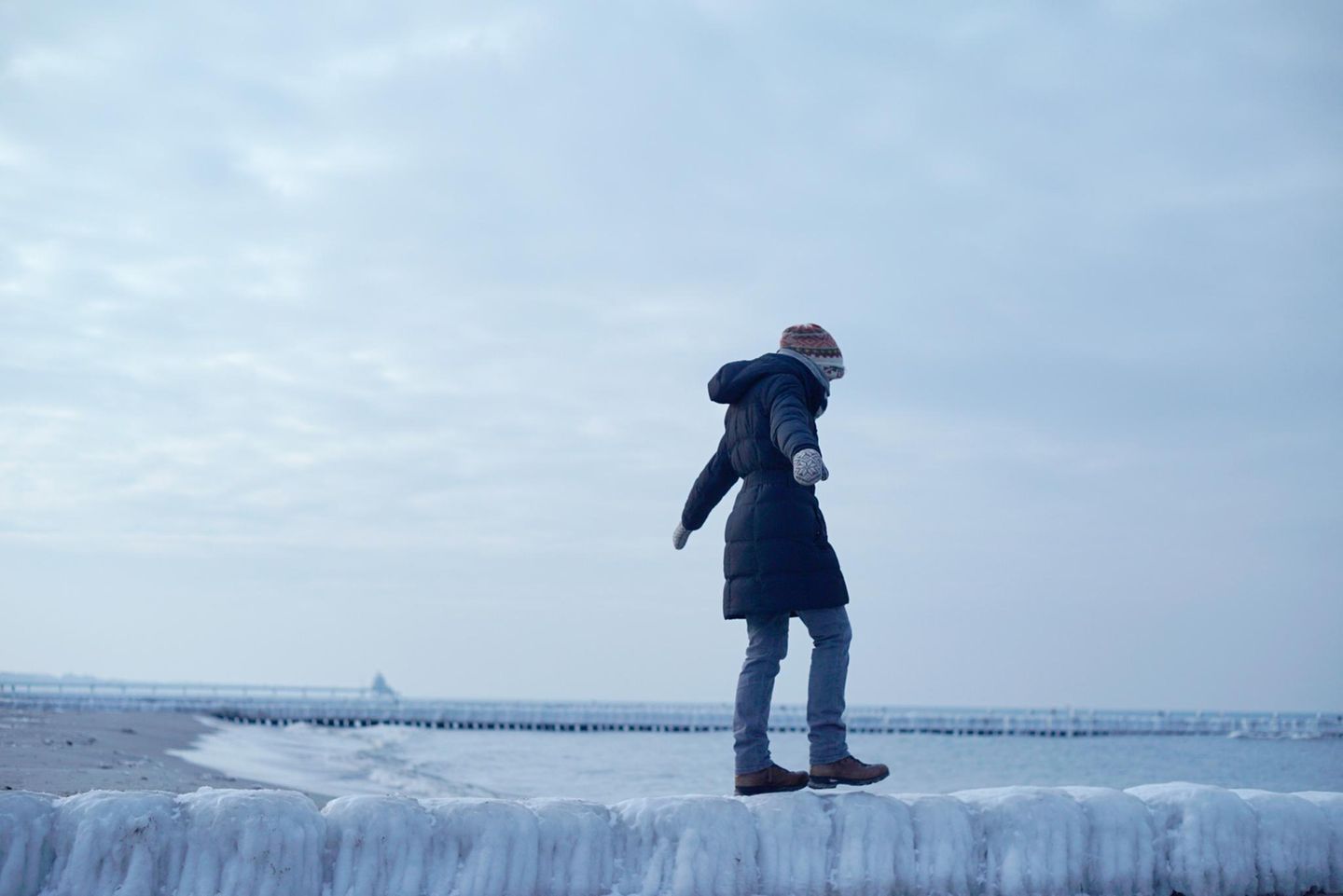 Frau balanciert unsicher auf einer glatten Buhne aus Eis am Meer