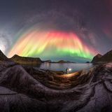 Milchstraße und rot bis grün verlaufendes Polarlicht über den Felsen der Inselkette der Lofoten