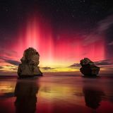 Zwei Felsen ragen aus dem Meer, der Nachthimmel leuchtet dahinter von gelb am Horizont bis tief violett