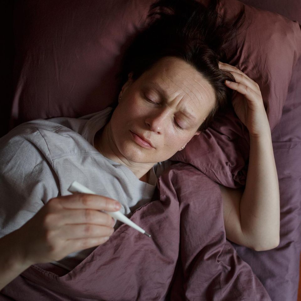Kranke Frau im Bett die auf ein Fieberthermometer schaut