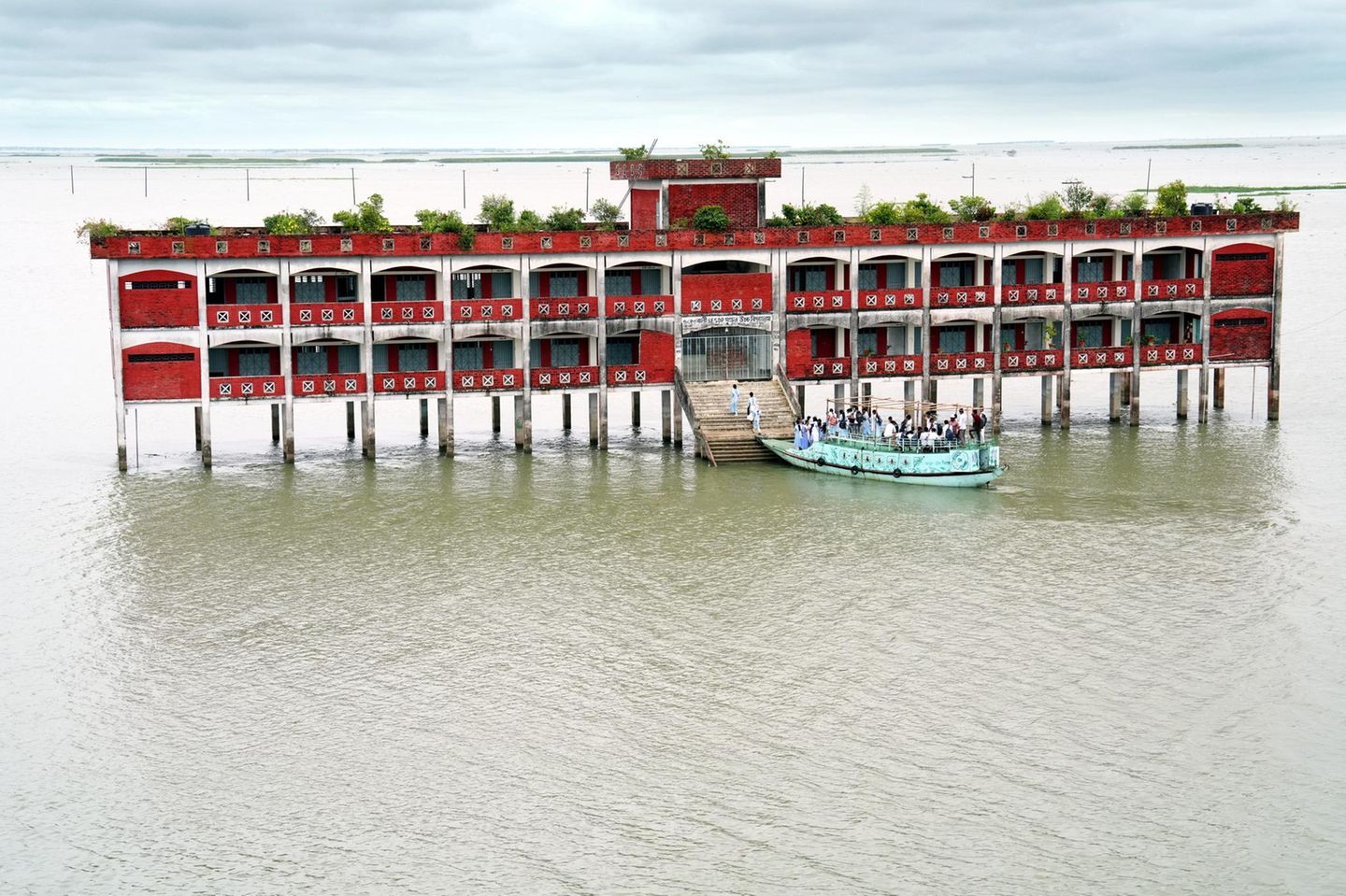 In den Haor-Feuchtgebieten von Kishoreganj, Bangladesch: Fast neun Monate im Jahr ist die Baherbali SESDP Model High School von Hochwasser umgeben und nur mit dem Boot erreichbar. Jeden Tag begeben sich 220 Schüler und zehn Lehrer aus sieben umliegenden Dörfern auf die Reise durch die überflutete Landschaft. Die auf Stelzen erbaute Schule gewährleistet, dass die Kinder trotz schwieriger Umweltbedingungen weiter lernen können.