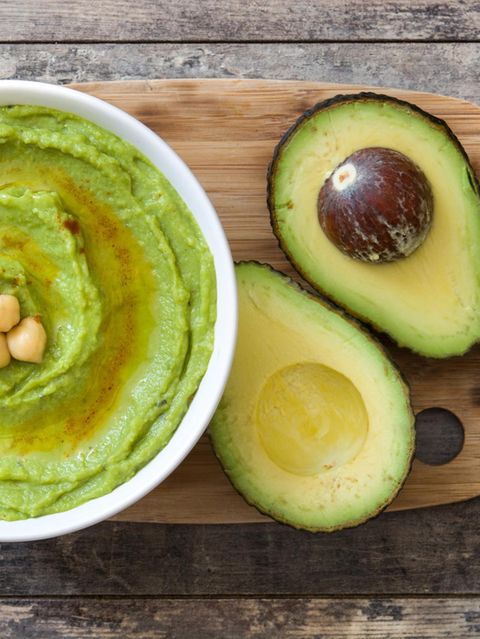 Aufgeschnittene Avocado auf einem Holzbrett imt Avocado-Hummus in einer Schüssel