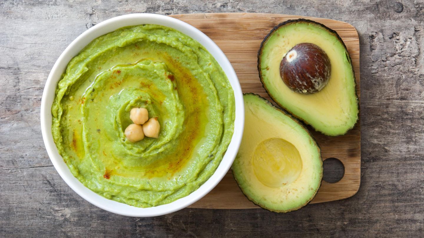 Aufgeschnittene Avocado auf einem Holzbrett imt Avocado-Hummus in einer Schüssel