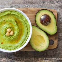 Aufgeschnittene Avocado auf einem Holzbrett imt Avocado-Hummus in einer Schüssel