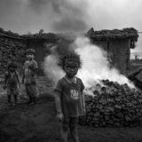 Ein Kind blickt in die Kamera: Es steht vor einem qualmenden Kohleberg