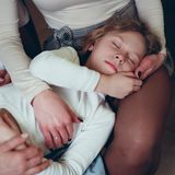 Ein Mädchen liegt, die Augen geschlossen, auf dem Schoß einer Frau