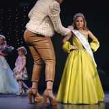 Ein Mädchen trägt Scherpe und Krone, dazu ein gelbes Kleid