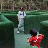 Ein Mädchen, aus ihrem rechten Hosenbein ragt eine Prothese, geht durch ein Heckenlabyrinth