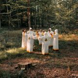 Die Atomianer tragen weiße roben, strehen im Kreis im Wald und halten sich an den Händen