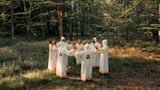 Die Atomianer tragen weiße roben, strehen im Kreis im Wald und halten sich an den Händen