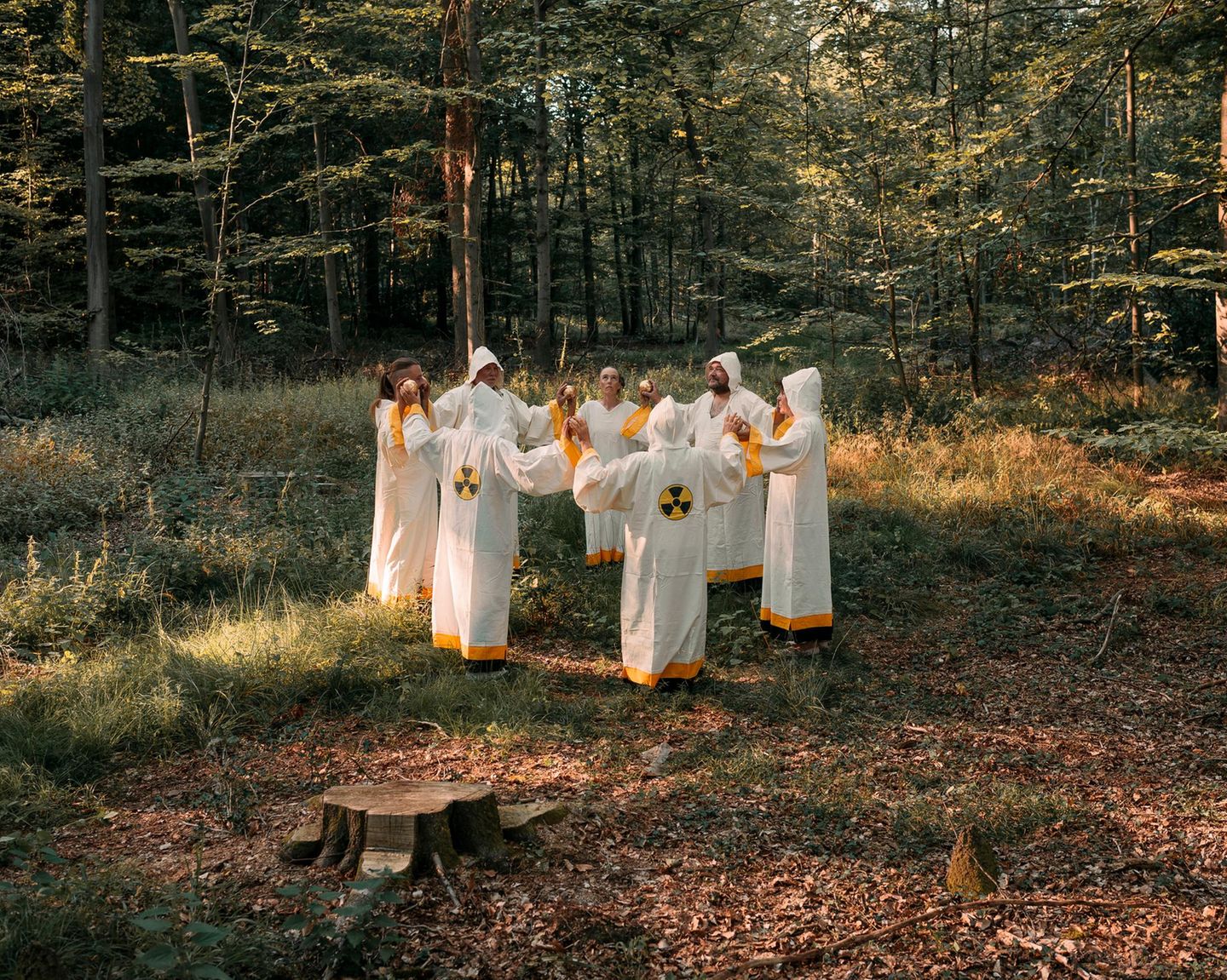 Die Atomianer tragen weiße roben, strehen im Kreis im Wald und halten sich an den Händen