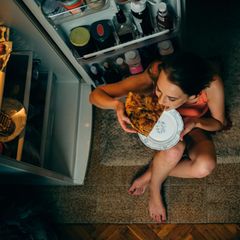 Frau isst spät in die Nacht vor dem Kühlschrank in der Küche Pizza
