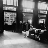 Eine Abfertigungshalle der Lufthansa mit Sesseln und Menschen vor Schaltern, schwarz-weiß Foto