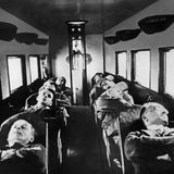 Acht Passagiere liegen auf umgelegten Sitzen in einer Flugzeugkabine, um 1930