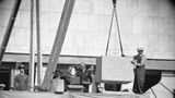 Ein gewaltiger Grundstein wird von einem Arbeiter in Position bugsiert; daneben Offizielle, sw-Foto 1949