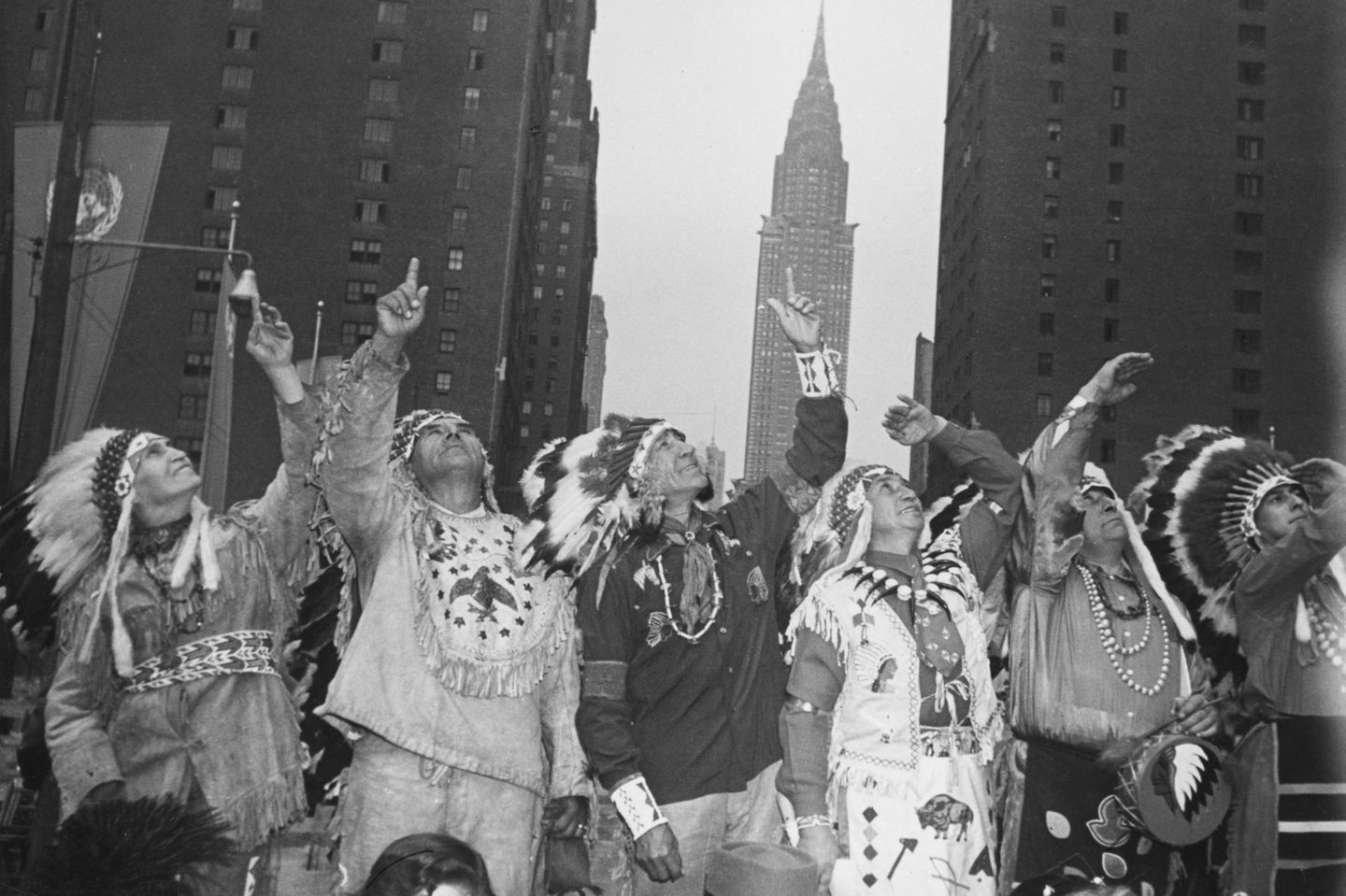 Sechs nordamerikanische Indigene in traditioneller Kleidung, die vor der Kulisse Manhattans in die Höhe schauen; sw-Foto; 1949