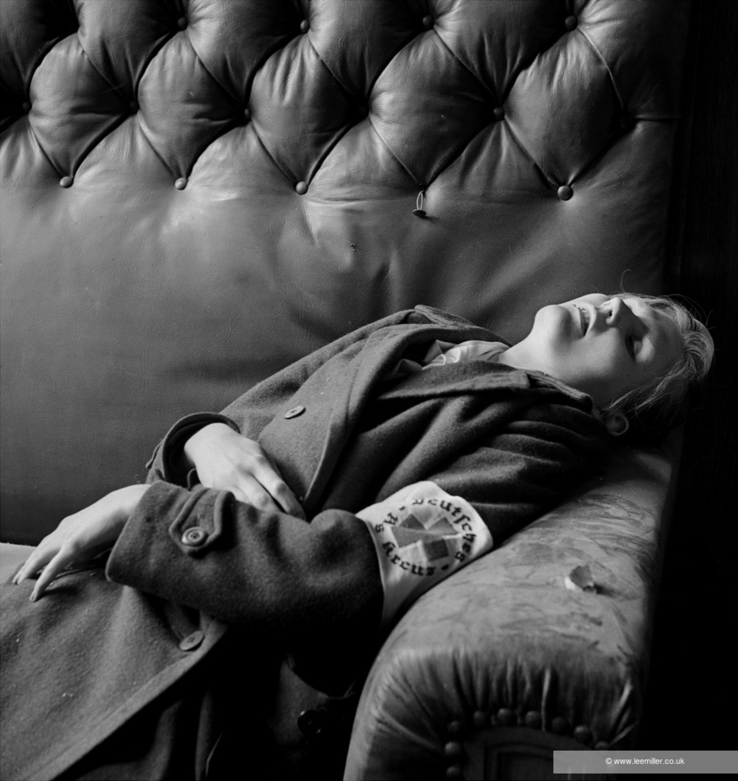 Eine junge Frau in einem Mantel, die Rot Kreuzbinde am Arm. liegt tot in einer Sofaecke, Schwarzweißfoto